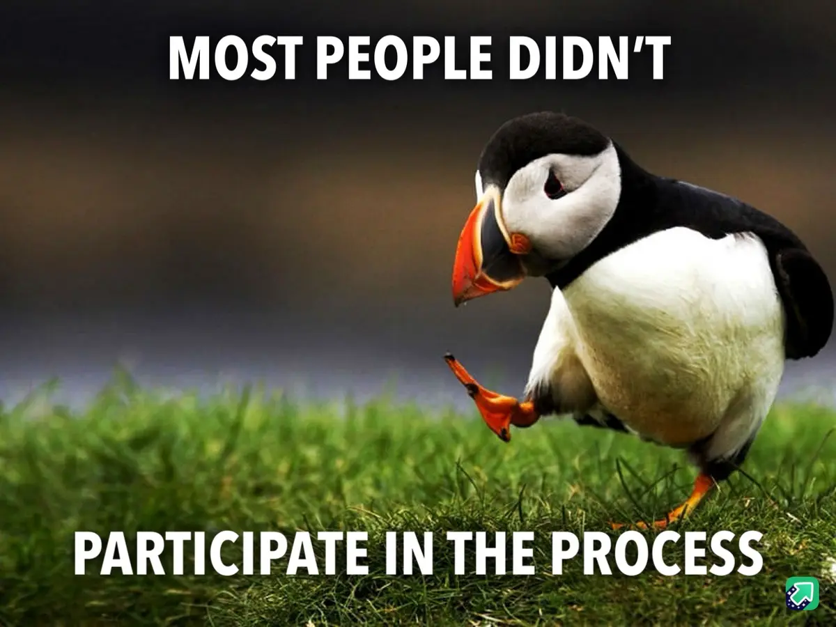 A close-up photograph of a puffin standing on green grass, looking down with a slightly dejected or unimpressed expression…