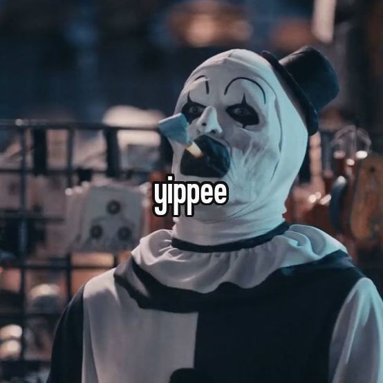 A person wearing a white and black clown costume with a painted face, a small black top hat, and a lit cigarette in their…