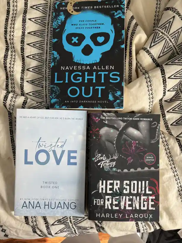 Three dark romance novels are laid out on a patterned blanket: 'Lights Out' by Navessa Allen (with a blue skull cover)…