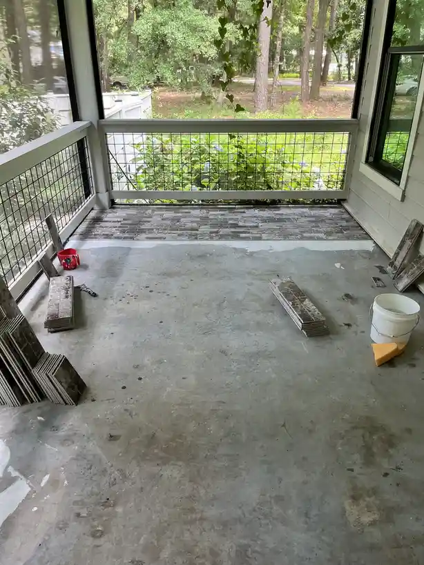 A partially tiled porch shows a stark contrast between the newly laid dark gray tiles in the back and the bare, unfinished…