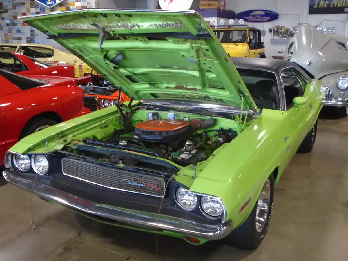 A lime-green classic Dodge Challenger RT with its hood open, revealing a rusty interior and engine bay, parked in a garage…