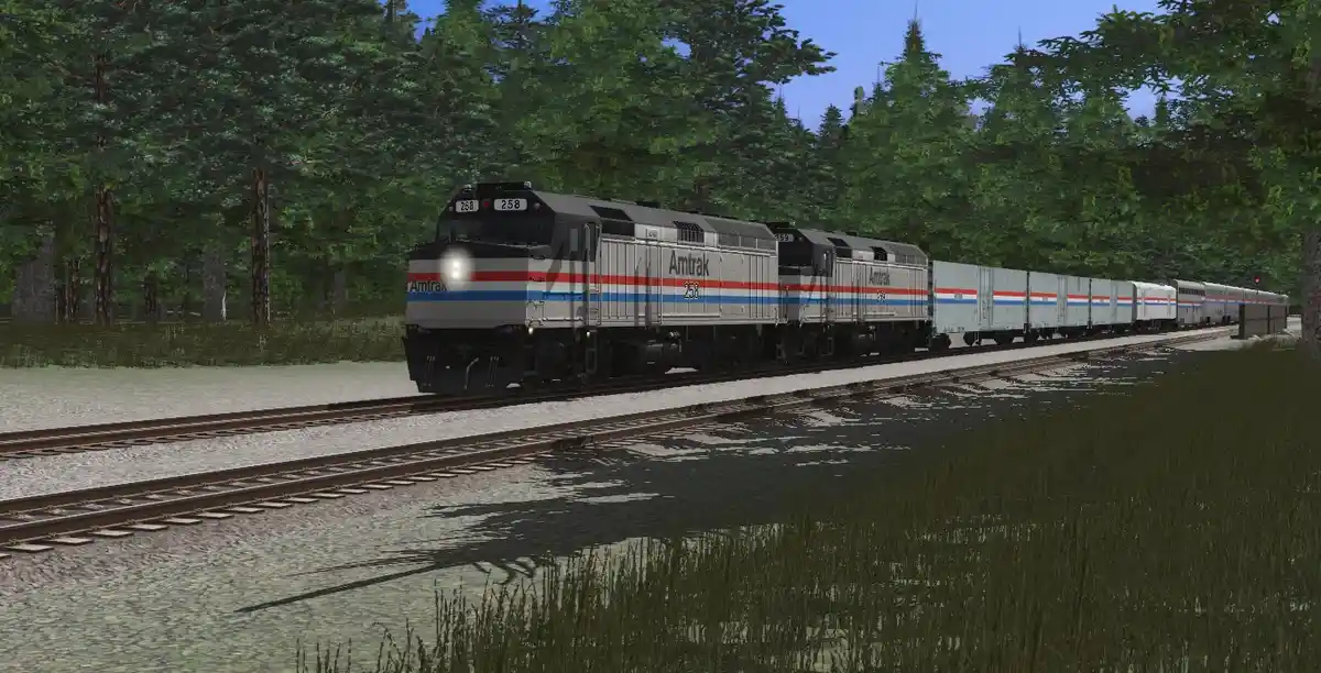 An Amtrak passenger train, led by locomotive number 258, travels through a forested area with trees on both sides of the…