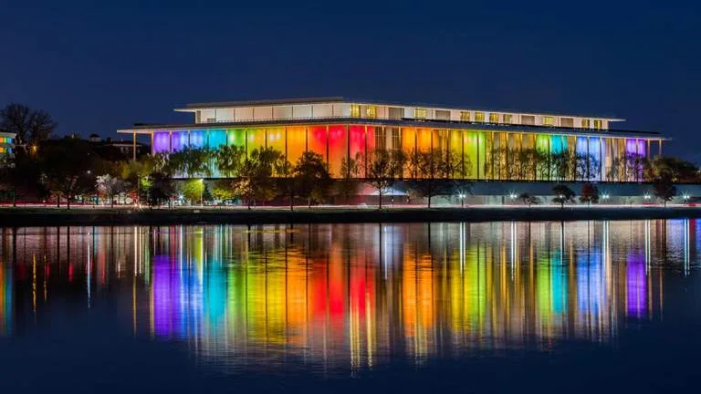 a modern building at night is illuminated with a full rainbow spectrum of lights across its facade, creating a vibrant…
