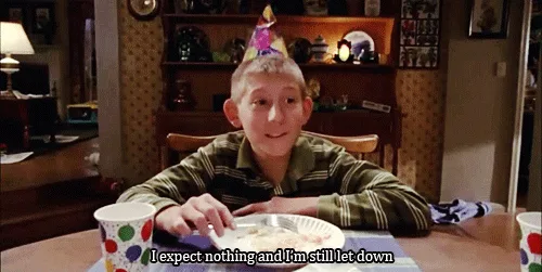 A young boy wearing a party hat sits at a dining table with a paper plate and cup, looking progressively more disappointed…