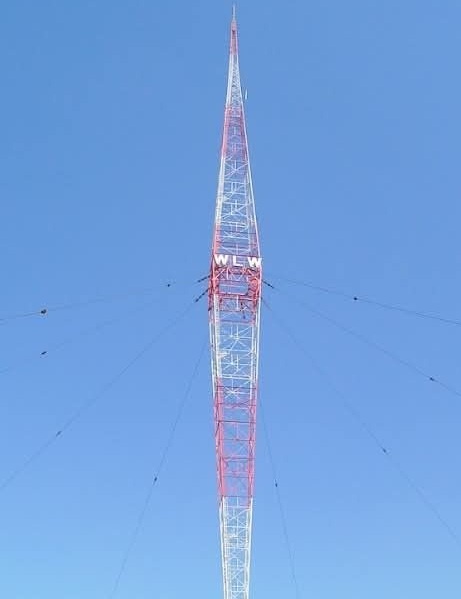 A tall, red-and-white lattice radio tower against a clear blue sky, with the letters 'WLW' prominently displayed on its…