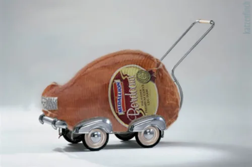 A whole, vacuum-sealed ham with a 'Bendict' brand label is mounted on a miniature, silver-colored toy car with four wheels…