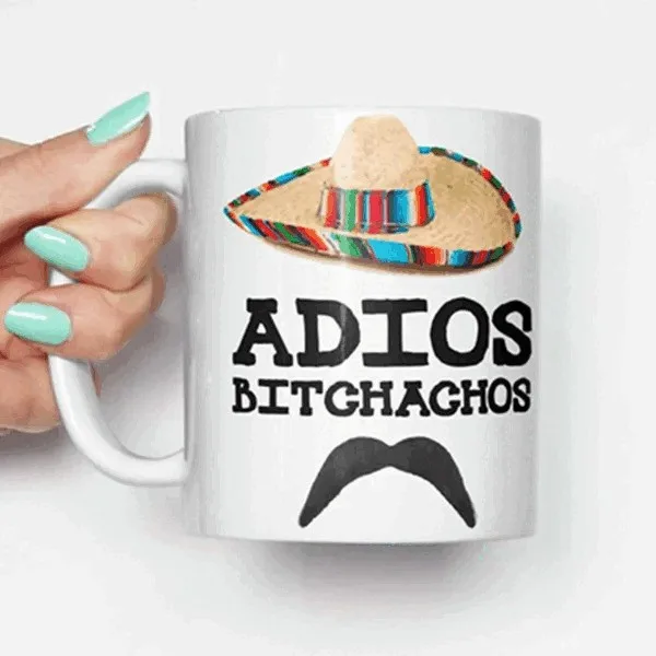 A white ceramic mug is held by a hand with light blue nail polish. The mug features a colorful sombrero graphic at the top…