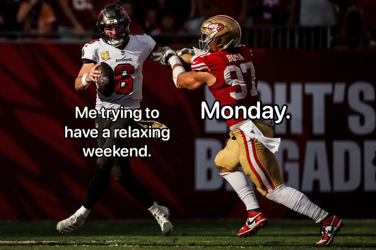 A Tampa Bay Buccaneers quarterback in a white jersey with the number 6 is holding a football and being tackled by a San…