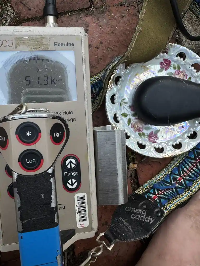 A close-up photo shows a handheld Eberline radiation detector displaying '5 1.3k cpm' on its screen, placed next to a…