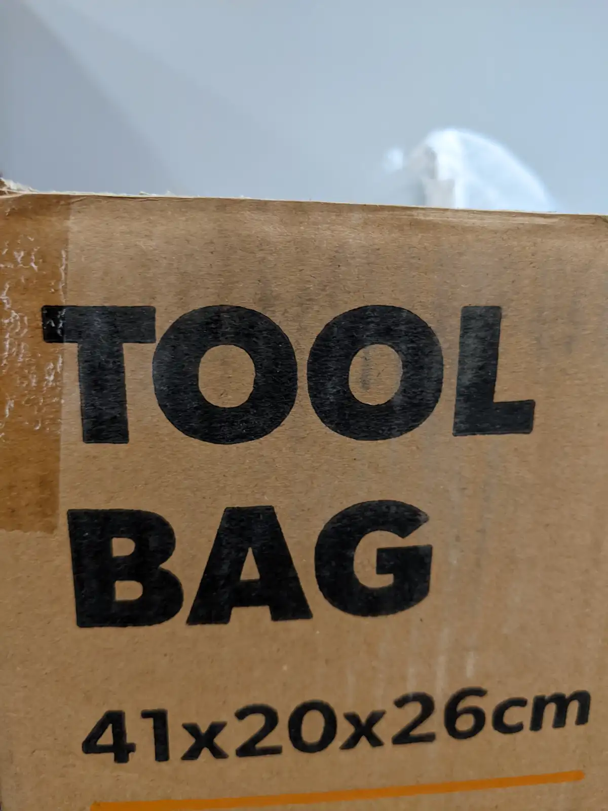 A close-up of a brown cardboard box labeled in bold black text as 'TOOL BAG' with dimensions '41x20x26cm' printed below. The…