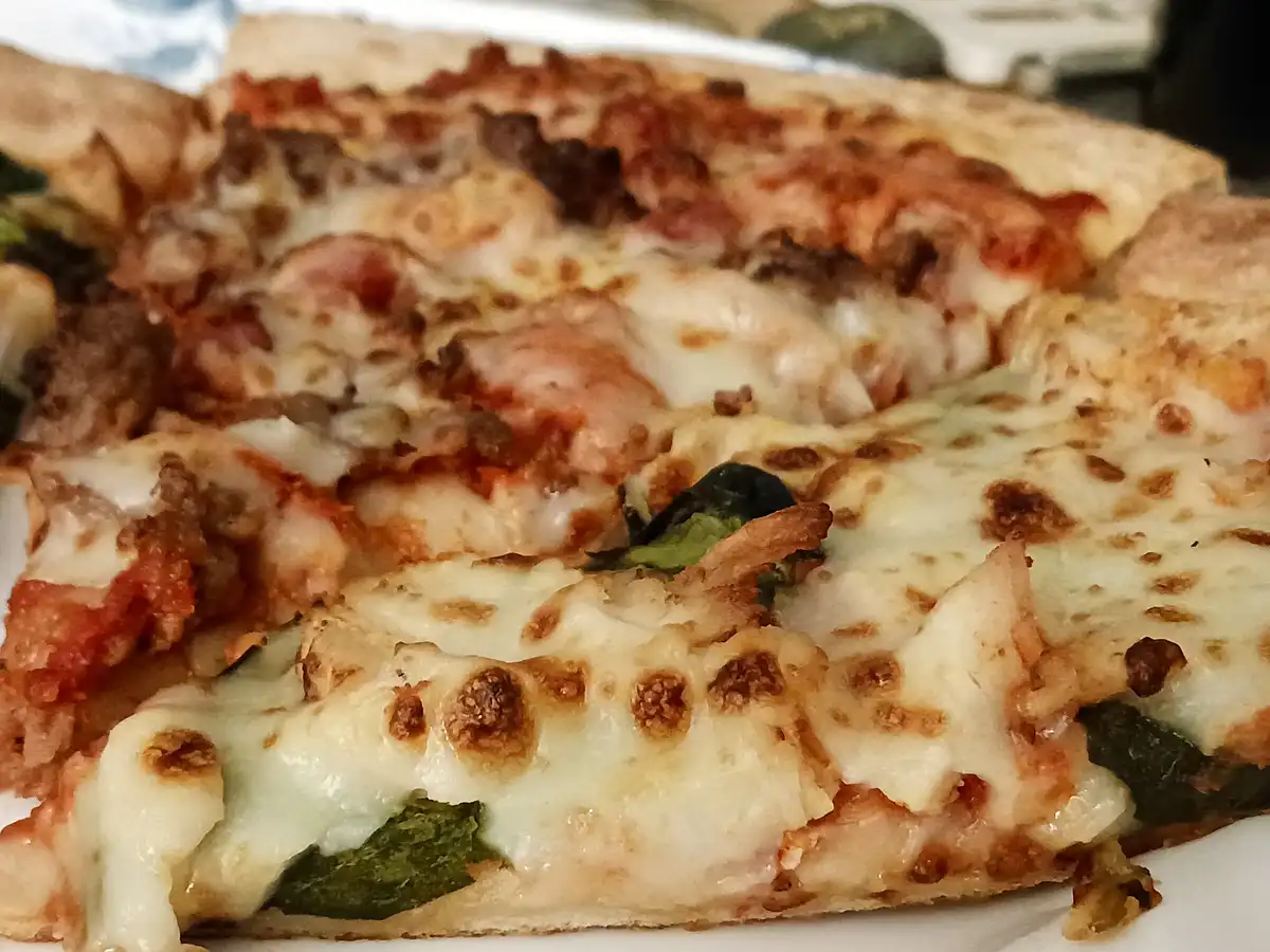 A close-up photo of several slices of pizza with melted cheese, tomato sauce, and green vegetable toppings on a white plate…