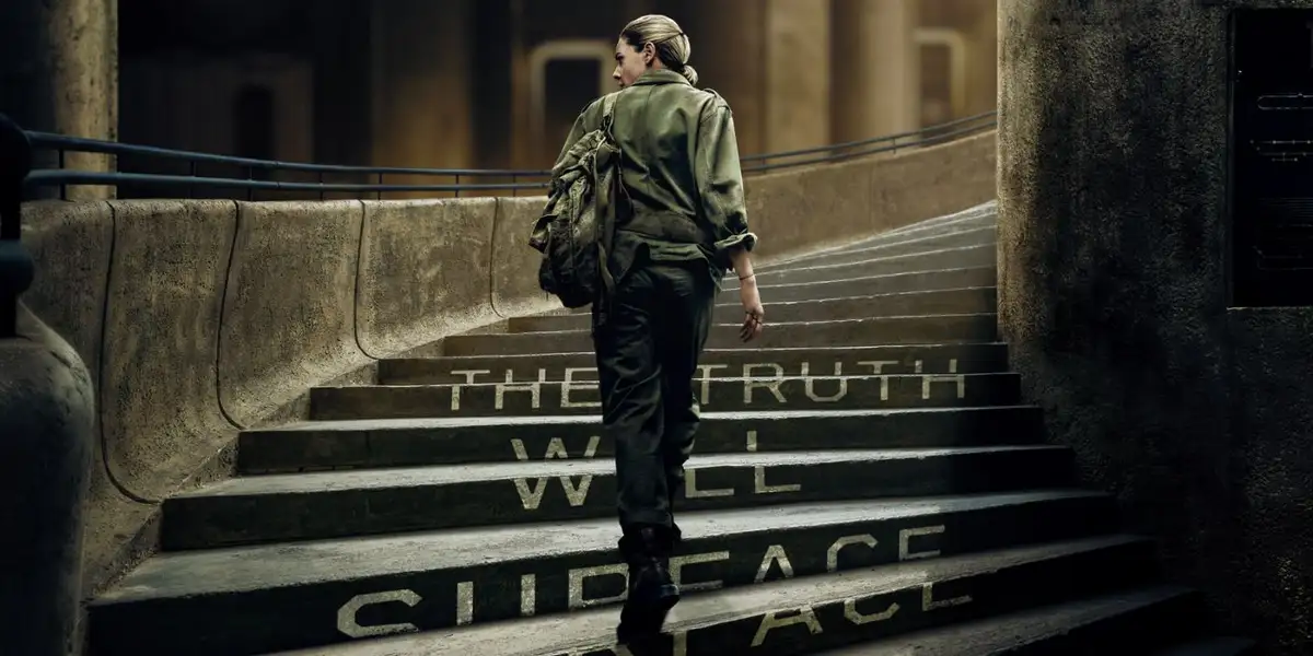A person in a green jacket and backpack walks up concrete stairs, with the words 'THE TRUTH WILL OUT' painted in white on…