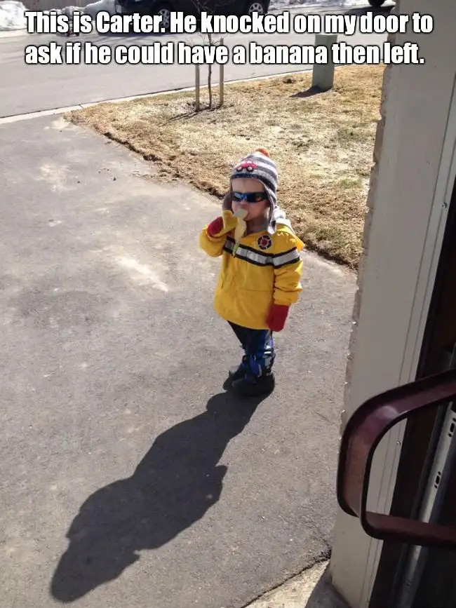 A young child named Carter, dressed in a yellow jacket, striped beanie, and sunglasses, stands on a sidewalk holding a…