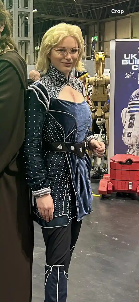 A person in a detailed Star Wars cosplay costume, featuring a blue velvet tunic with silver trim and studded sleeves, stands…