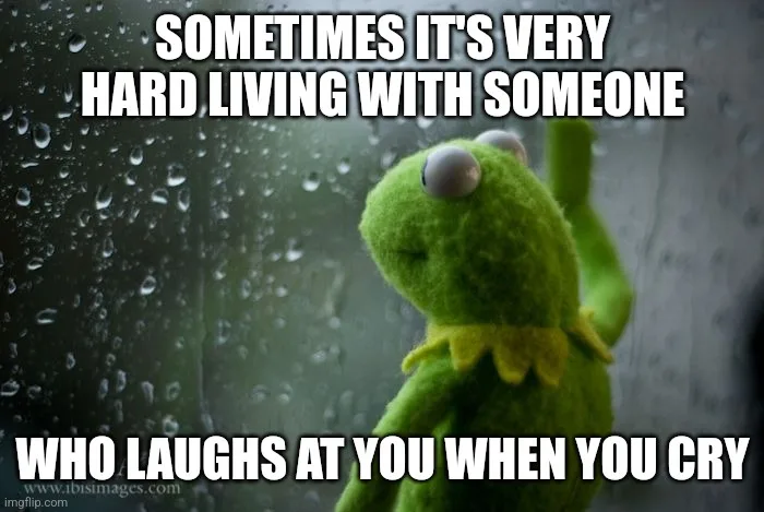 A green felt frog puppet, Kermit the Frog, is shown looking sad and contemplative while pressing his hand against a…