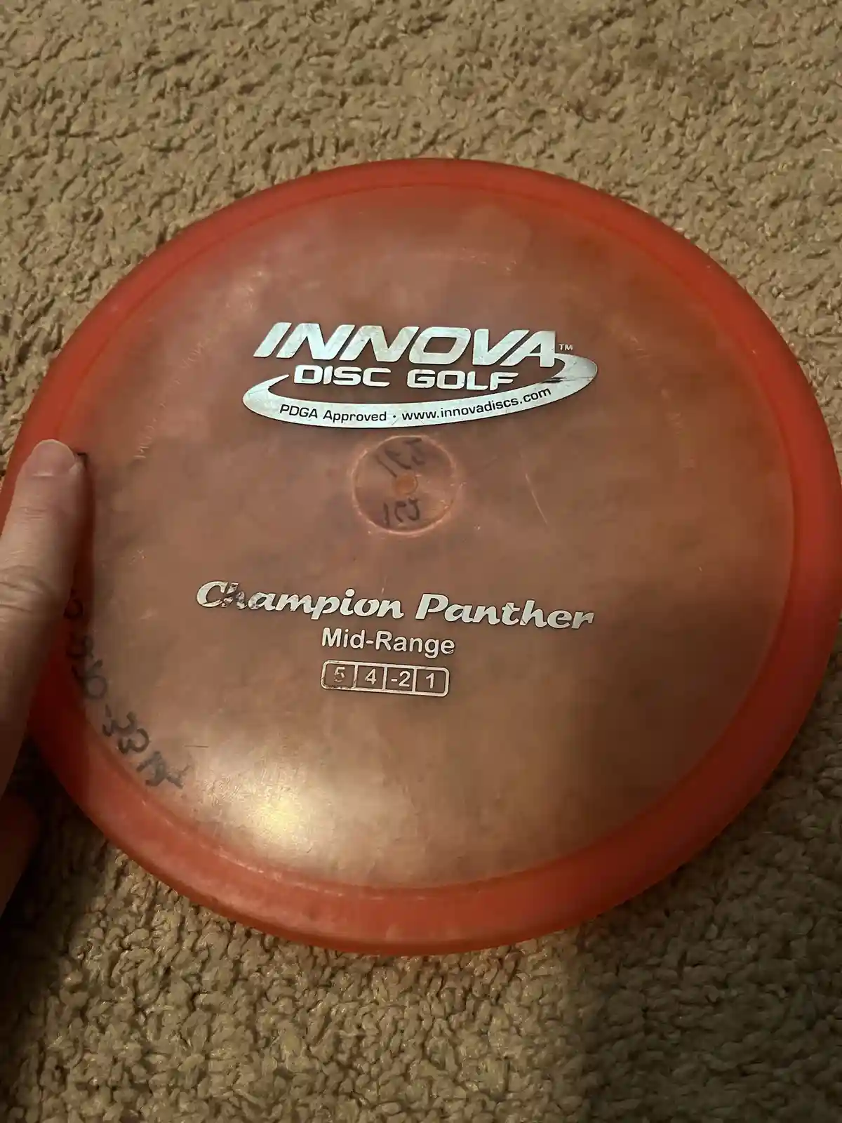 A close-up photo shows a worn, orange Innova Disc Golf disc labeled 'Champion Panther Mid-Range' with flight numbers '5 4 -2…