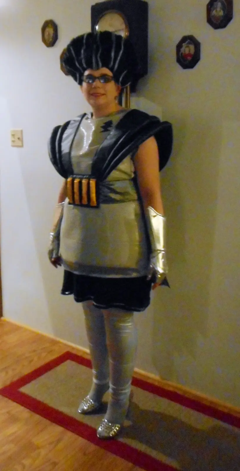 A person stands indoors wearing a full costume resembling a character from Star Wars, complete with a large black headdress…