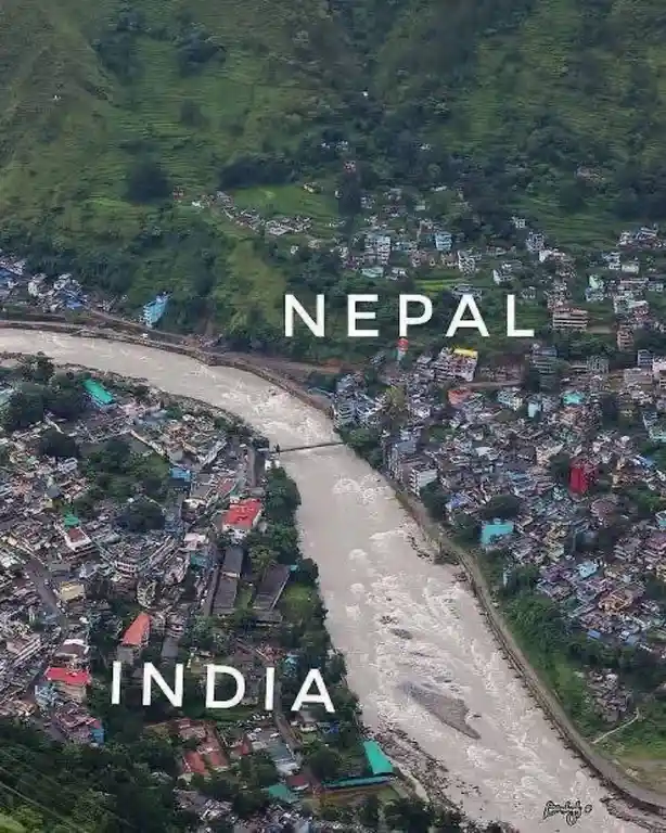An aerial photo shows a river dividing two densely built-up areas on opposite banks, with the word 'NEPAL' overlaid on the…